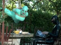MistTube presents: Girl in green latex hangs over table outdoors